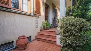 A house with a tiled patio, a large pot, and a staircase leading to the entrance.