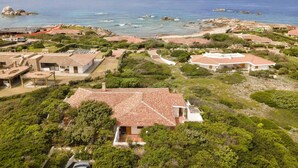 Una zona costiera con edifici tradizionali, una spiaggia e affioramenti rocciosi.