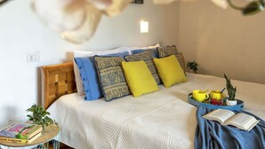 Camera da letto ordinata con un letto, cuscini, un comodino con un libro, una piccola pianta e un vassoio con tazze e una pianta.