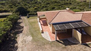 A house with a tiled roof, a patio with a table and chairs, and a view of the sea and hills in the background.