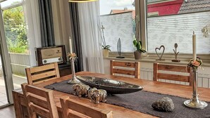 A dining area with a wooden table, chairs, and a large window with blinds. - Beautiful apartment for 2 people with WIFI, TV and terrace (Bad Pyrmont)
