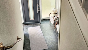 A hallway with a dark door, a star-shaped hanging light fixture, a patterned rug, and a chair with a white cushion. - Beautiful apartment for 2 people with WIFI, TV and terrace (Bad Pyrmont)