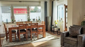 A dining area with a wooden table and chairs, a sofa, and a large window with curtains. - Beautiful apartment for 2 people with WIFI, TV and terrace (Bad Pyrmont)
