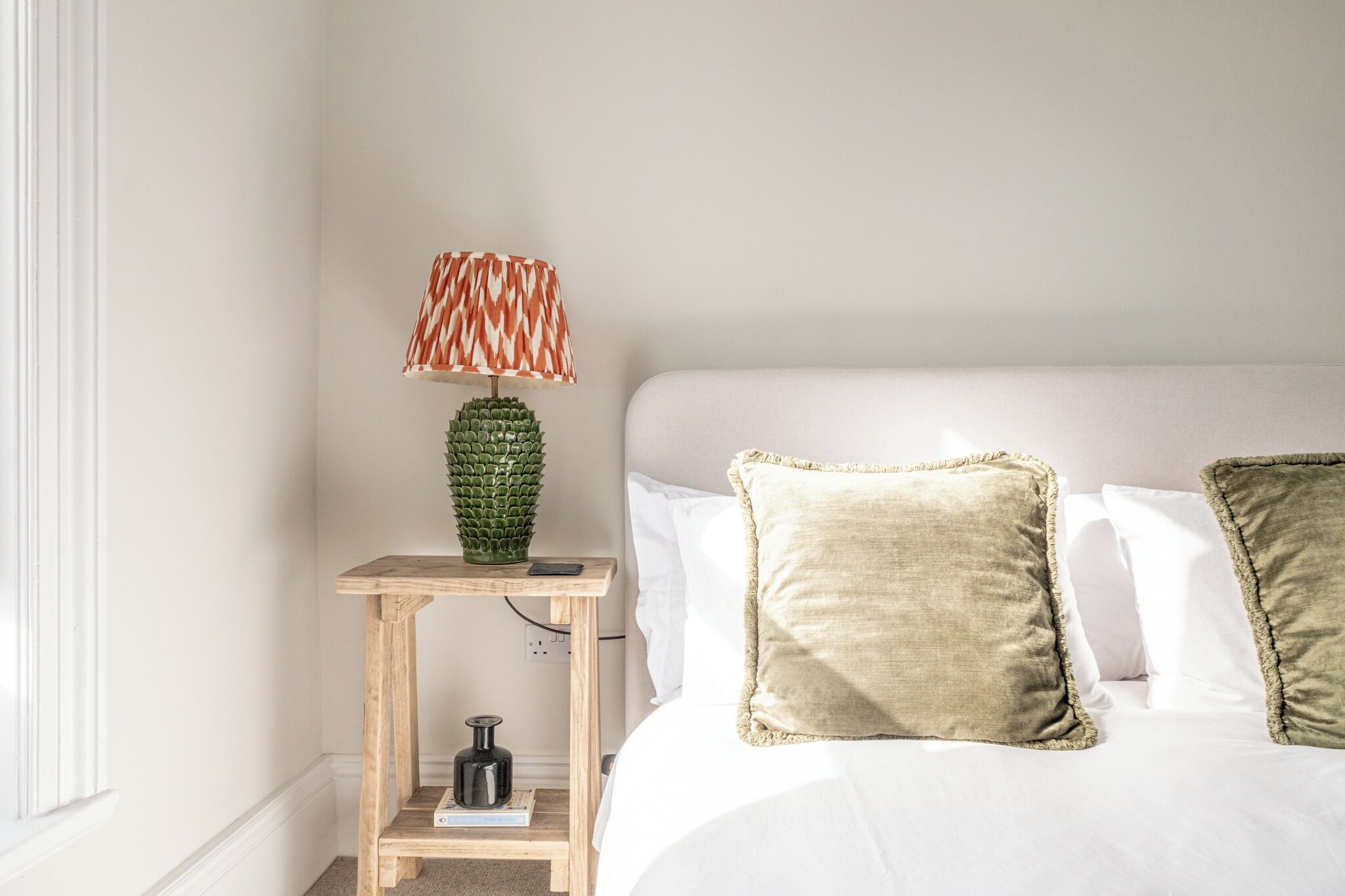 A neatly arranged bedroom with a bed, pillows, a lamp, and a small wooden nightstand.