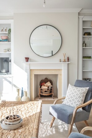 Un salon avec une cheminée, un miroir rond et un fauteuil bleu.