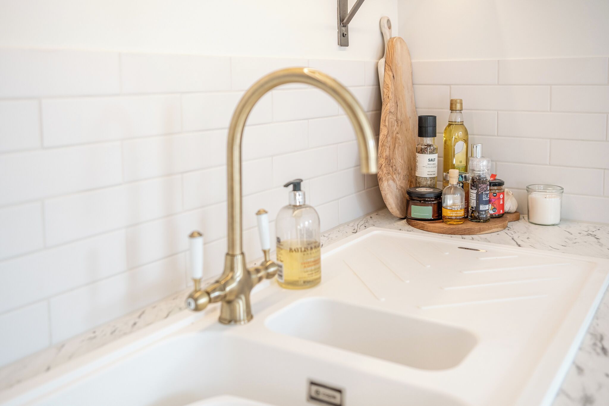 Una cocina con un lavamanos blanco, un grifo dorado y varios utensilios de cocina sobre la encimera.