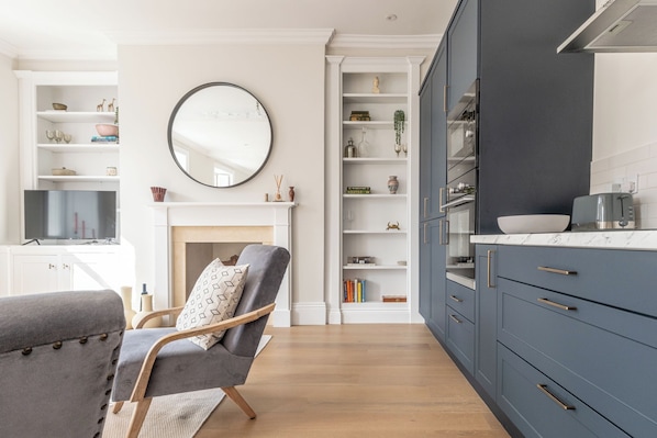 A modern kitchen with dark blue cabinets, a white fireplace, and a round mirror on the wall. - Hitchmans Mews - 2BD in Chipping Norton (Chipping Norton)