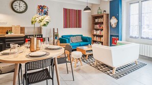 A modern living room with a dining area, a bookshelf, and a kitchen in the background. - Wonderful  villa for 5 people with WIFI and pets allowed (La Richardais)