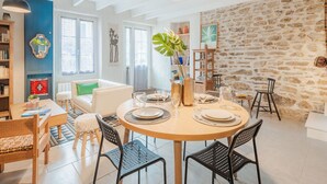 A dining area with a round table set for four, surrounded by black chairs. There is a bookshelf to the left and a stone wall to the right. - Wonderful  villa for 5 people with WIFI and pets allowed (La Richardais)