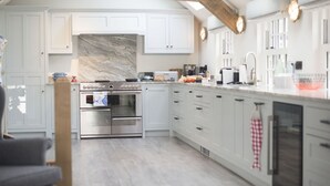 Une cuisine moderne avec des meubles blancs, un grand îlot central et un pare-feu en pierre.