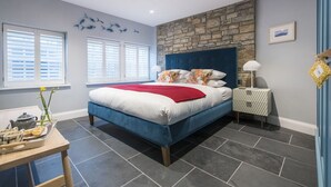 Une chambre avec un mur d’accent en pierre, un lit avec un couvre-lit rouge et une table de chevet avec une lampe.