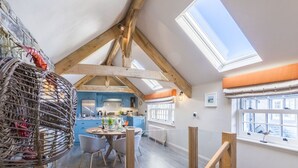 Un'ampia cucina con mobili blu, un'area pranzo con un tavolo rotondo e sedie, e un soffitto alto con lucernari.