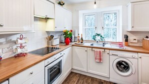 Cocina moderna con armarios blancos, encimera de madera, horno empotrado, lavadora y ventana con vidrio esmerilado.