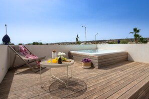 A wooden deck with a lounge chair, a small table with drinks and flowers, and a hot tub. - Villa IL Melograno 4 2 Emma Villas (Ragusa)