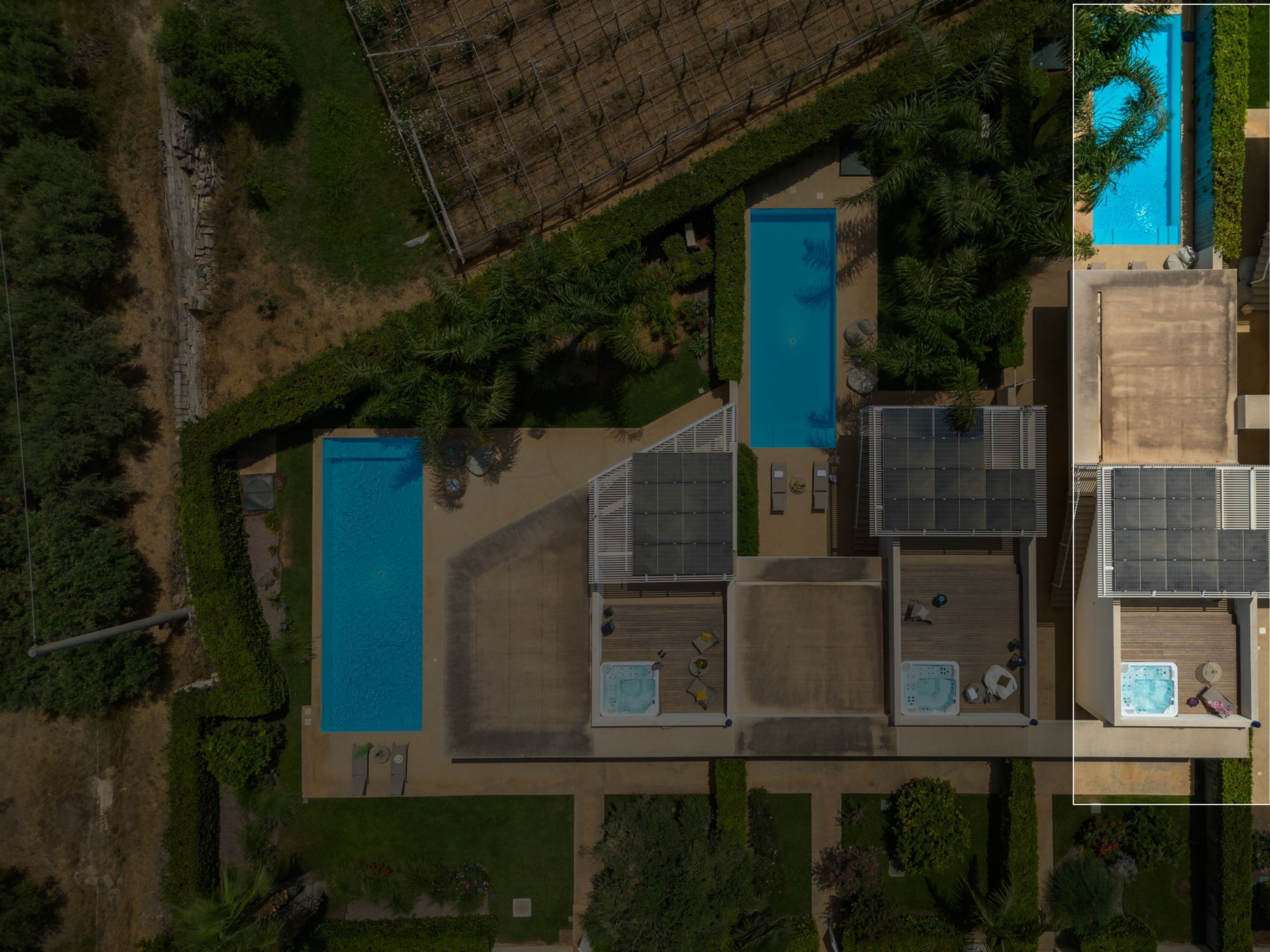An aerial view of a property with two swimming pools, a rooftop terrace with solar panels, and a well-maintained garden.