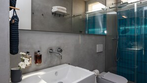 Egy modern fürőszoba, melyben egy nagy tükör, egy fehér kád, egy WC és egy üvegfalas zuhanyzó található.
