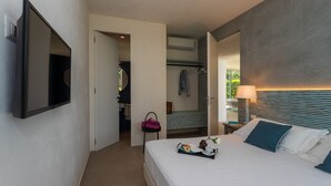 A modern hotel room with a large bed, bedside table, lamp, and a flat-screen TV mounted on the wall.