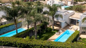 A modern resort with two swimming pools, palm trees, and a view of the sea.