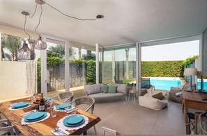 Comedor con mesa de madera preparada para cuatro personas, sofá y vista a la piscina.