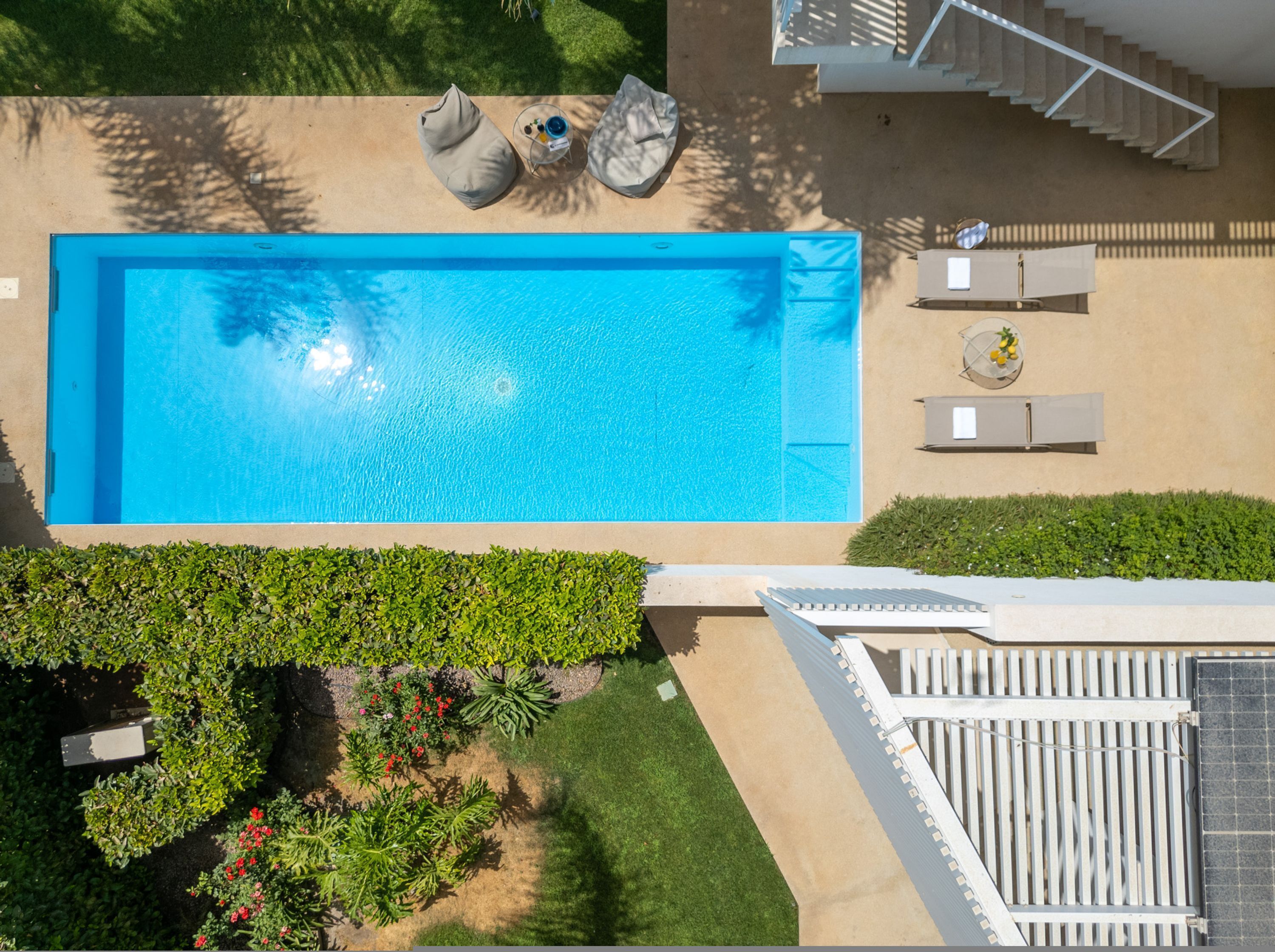An aerial view of a swimming pool with surrounding greenery and a white fence.