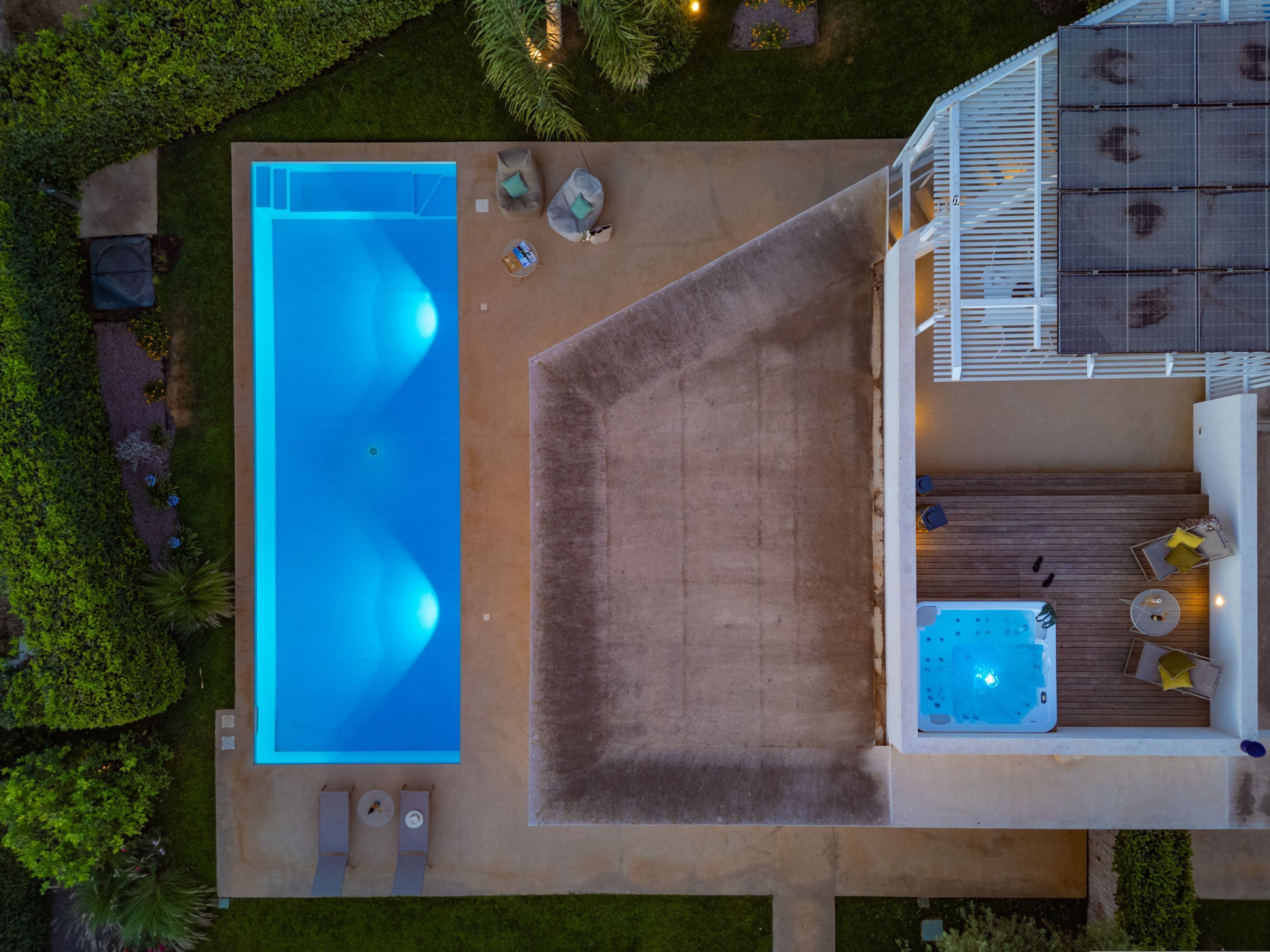 An aerial view of a modern house with a large rectangular swimming pool, a hot tub, and a deck area with outdoor furniture.