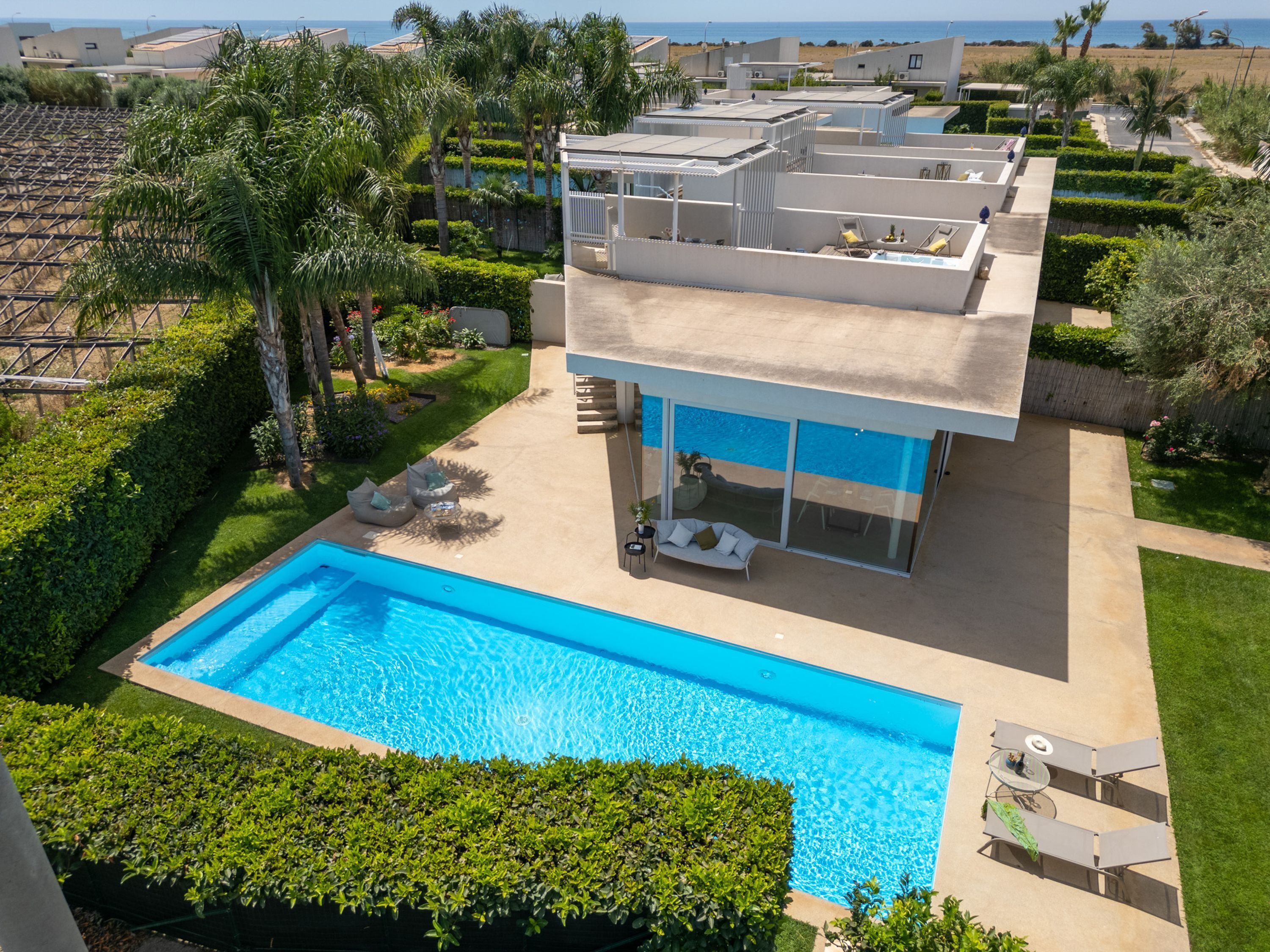 A modern two-story house with a swimming pool, outdoor seating, and a view of the ocean.