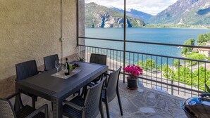A balcony with a table and chairs, a potted plant, and a view of a lake and mountains. - Beautiful  villa for 5 guests with WIFI, TV and terrace (Verceia)