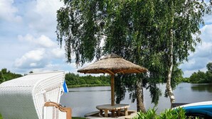 Søudsigt med parasol af strå, et picnicbord og en overdækket siddeplads.