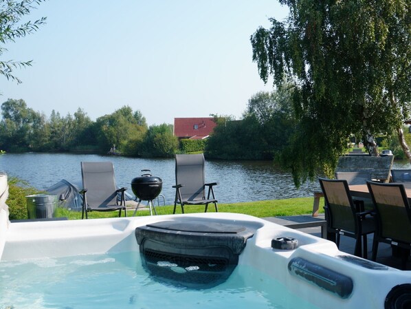 A hot tub with a view of a lake, surrounded by chairs and a grill.