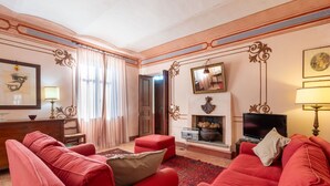 Un salon avec des canapés rouges, une cheminée, un téléviseur et une grande fenêtre avec des rideaux.