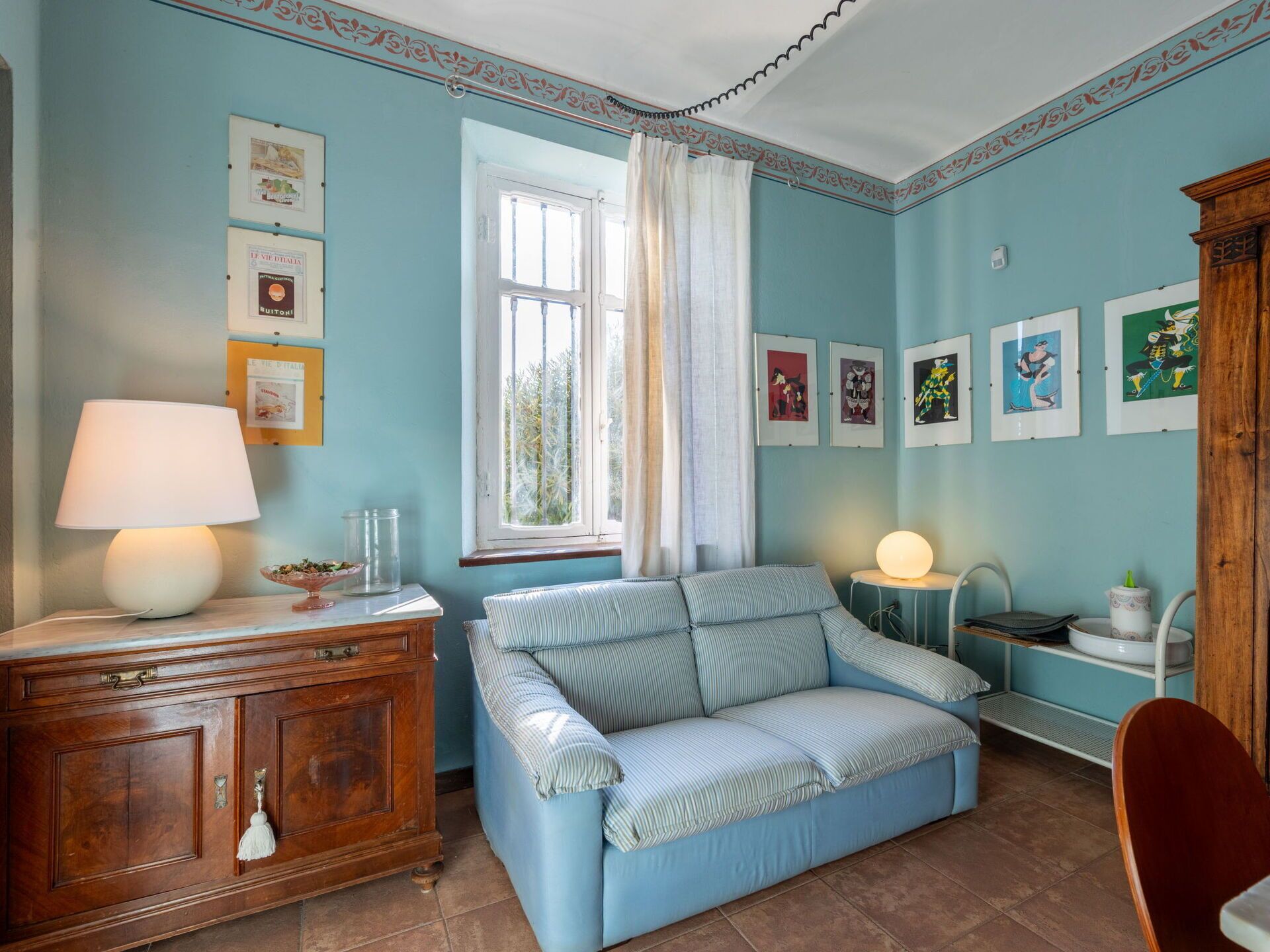 A room with a blue sofa, a wooden cabinet, a lamp, and framed pictures on the wall.