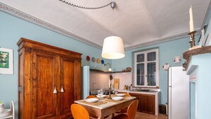 Une cuisine avec des meubles de rangement en bois, une table à manger avec des chaises, un luminaire suspendu et un réfrigérateur.