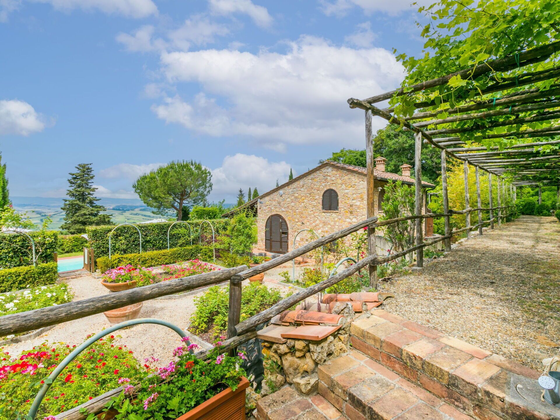 A stone building with a garden and a pergola with vines.