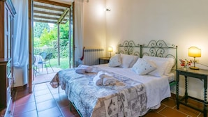 A bedroom with a bed, a nightstand, a lamp, and a view of the garden through an open door. - Stunning  villa for 16 guests with WIFI, private pool, A/C, TV and panoramic view (Montaione)