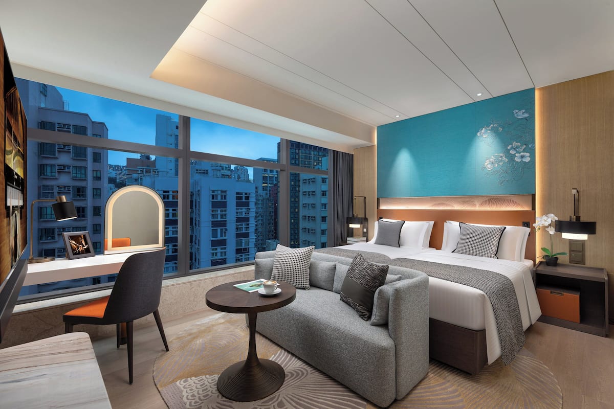 Un hotel moderno con una cama grande, un sofá, un escritorio y vistas de la ciudad a través de amplios ventanales.