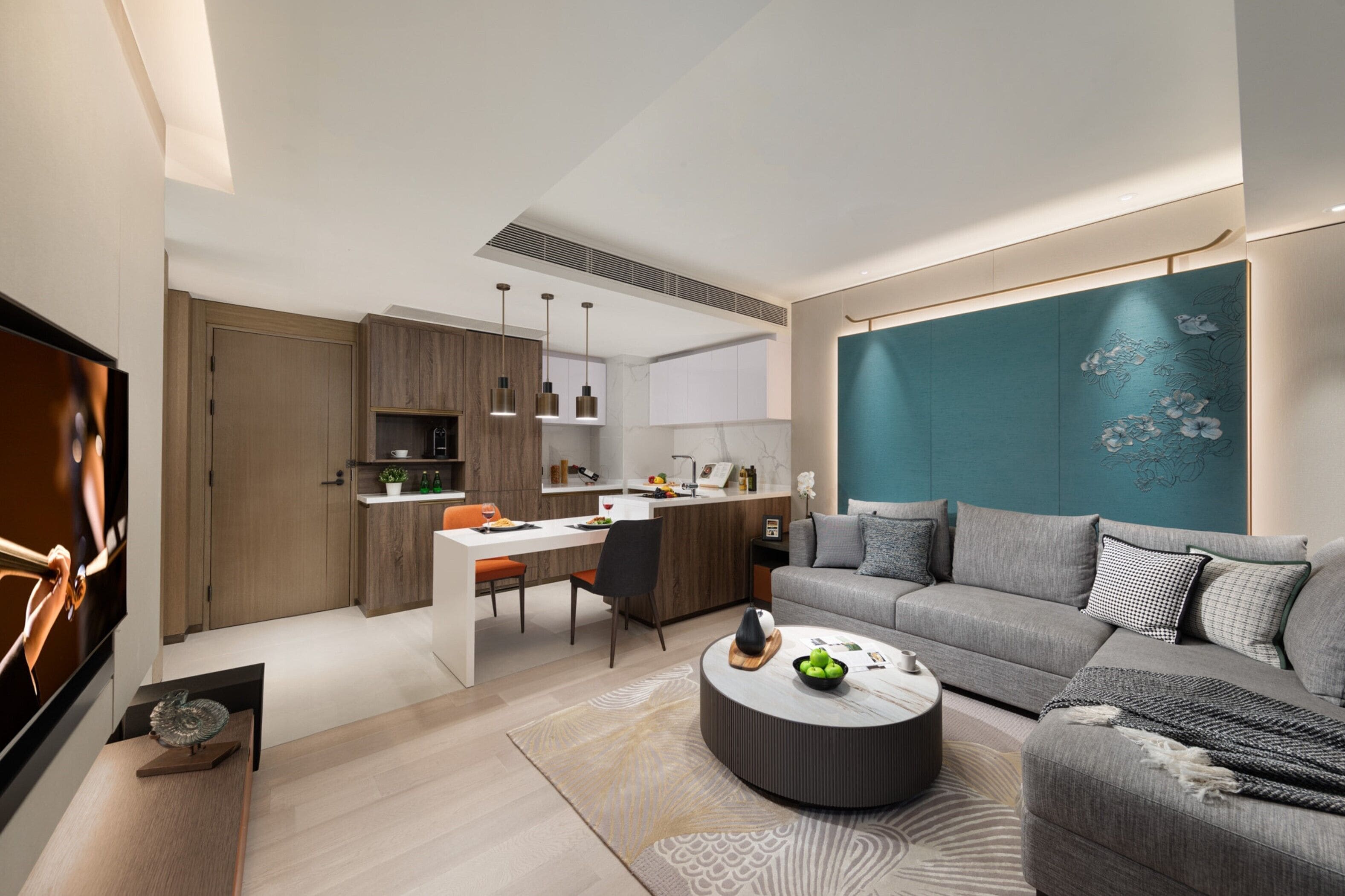 A modern living room with a grey sofa, a coffee table, and a dining area with a kitchen in the background.