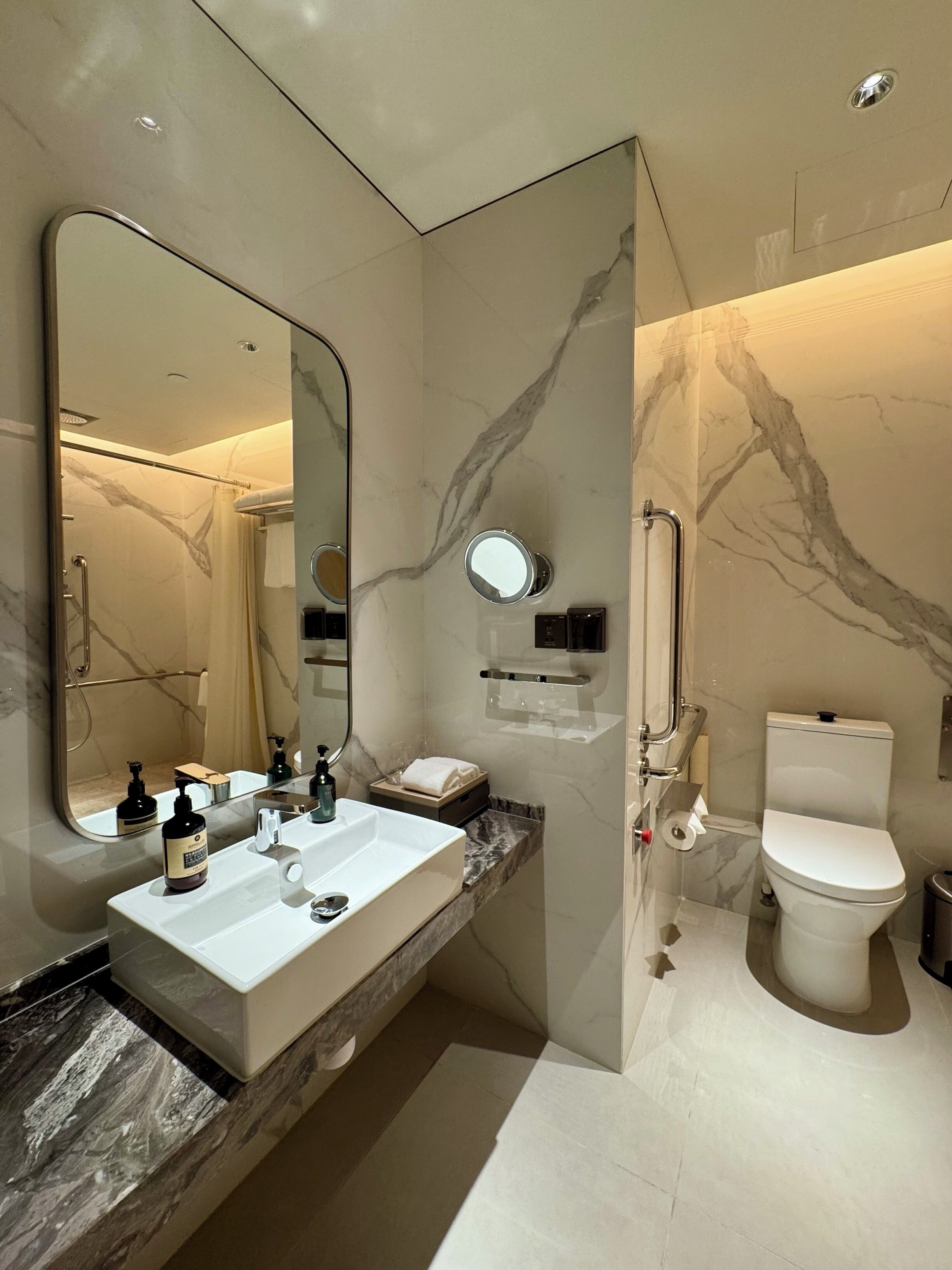 A modern bathroom with a large mirror, a white sink, a toilet, and a shower area.