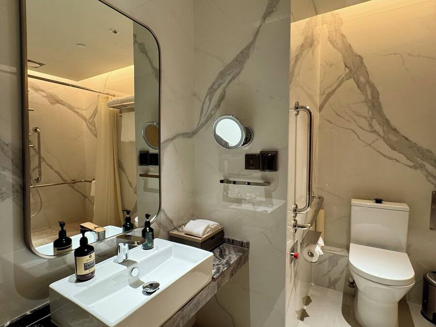 A modern bathroom with a large mirror, a white sink, a toilet, and a shower area.