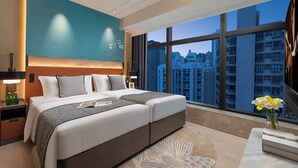 Un dormitorio de hotel moderno con una cama grande, una mesita de noche, una lámpara y vistas a la ciudad a través de amplios ventanales.