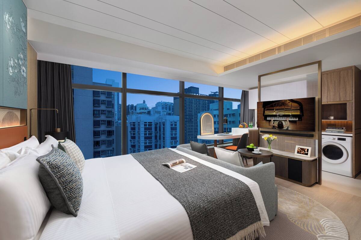 Habitación de hotel moderna con una cama grande, un escritorio, una lavadora y vistas a la ciudad.