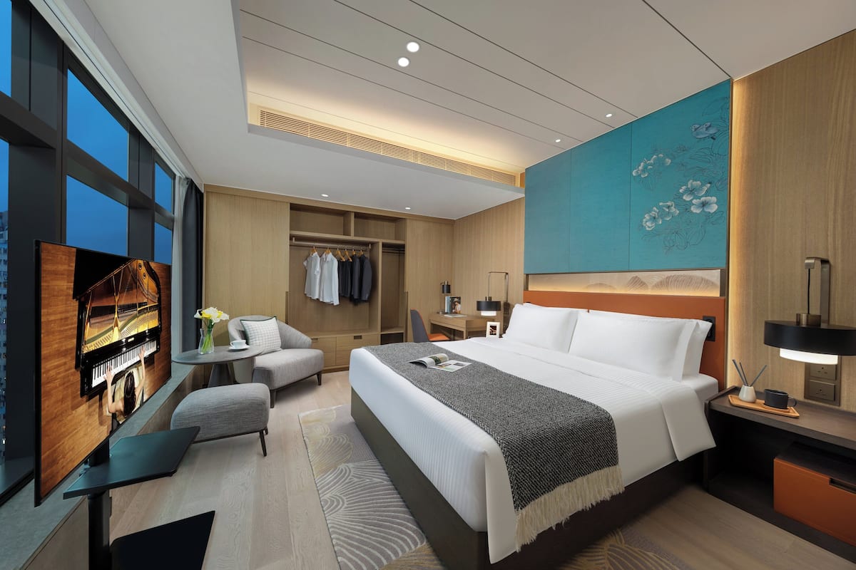 Habitación de hotel moderna con una cama grande, un escritorio, una zona de estar y vistas a la ciudad.