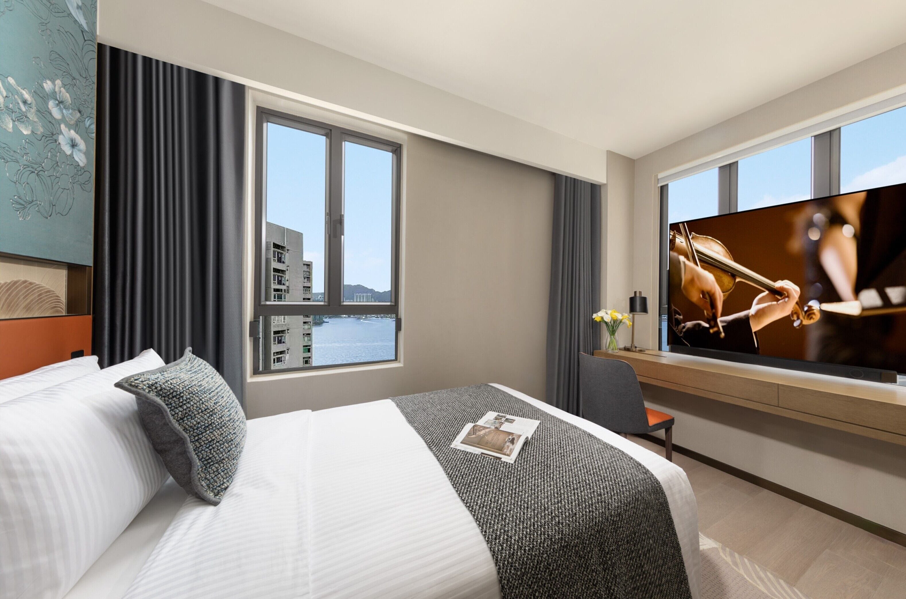A hotel room with a large bed, a television, a desk, and a window with a city view.