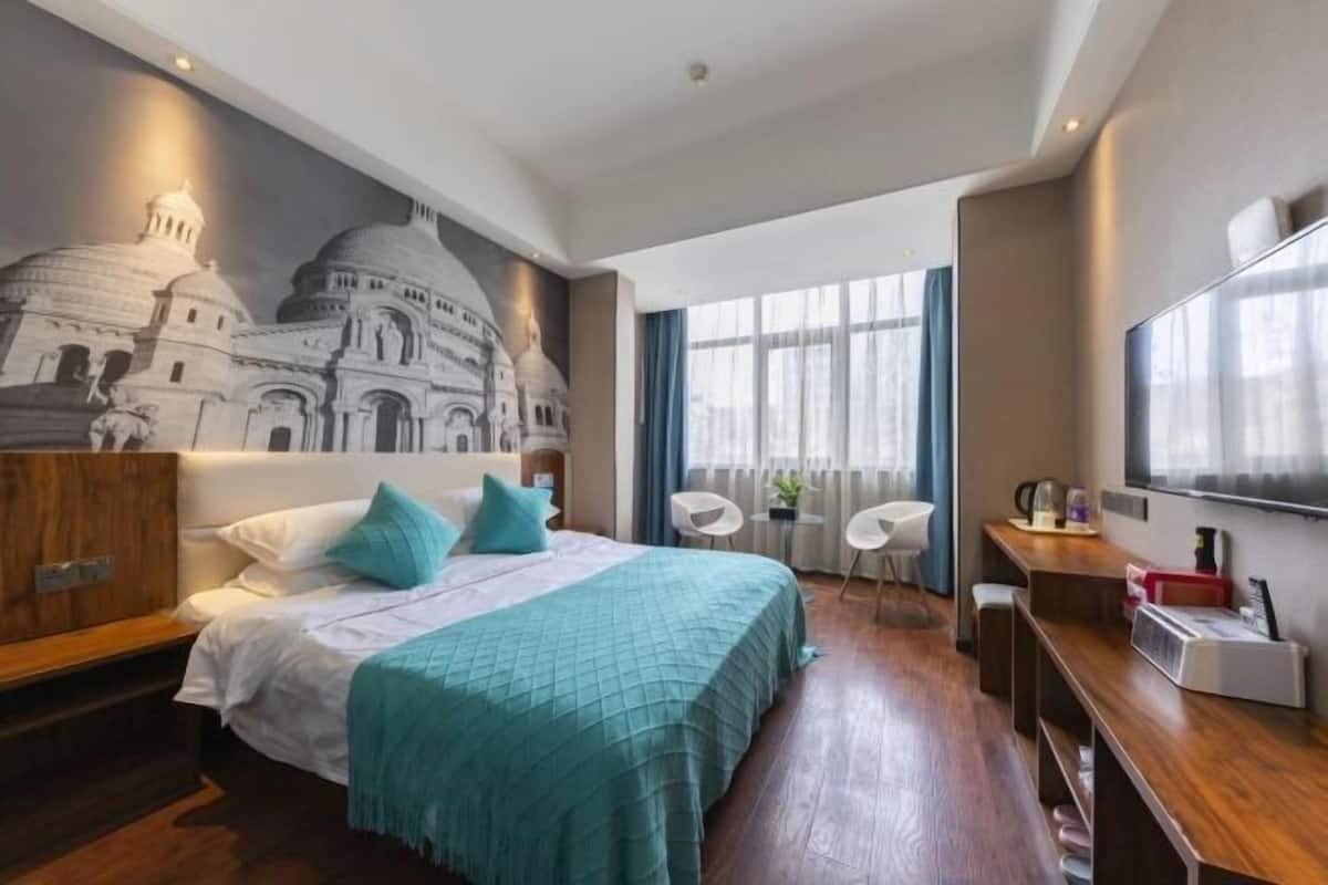 Habitación de hotel con cama, escritorio, silla, televisor y un mural de un edificio.