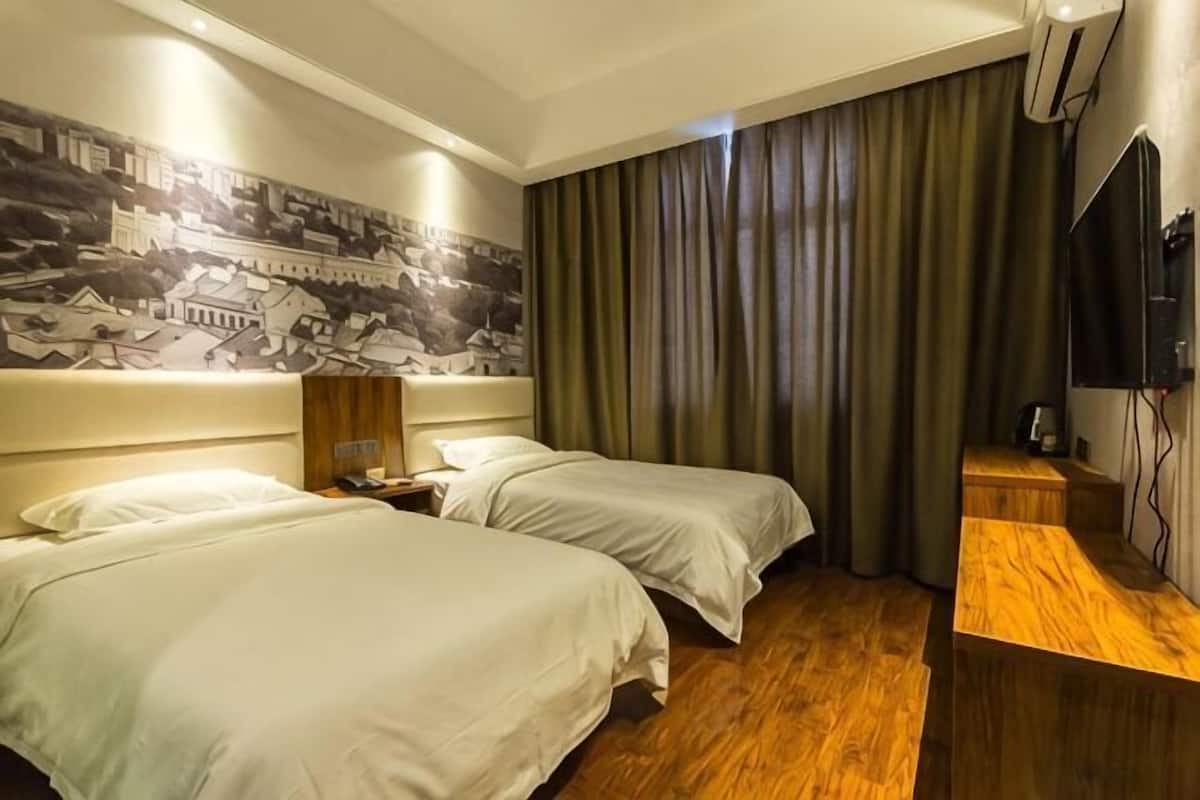 Habitación de hotel con dos camas, un escritorio de madera, un televisor de pantalla plana y un mural en la pared.