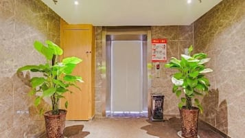Um hall de hotel com piso de mármore, porta de madeira e duas plantas em vasos.