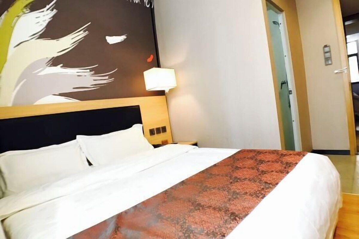 Une chambre d’hôtel avec un lit, une table de chevet, un mur orné d’un tableau, une porte et un luminaire.