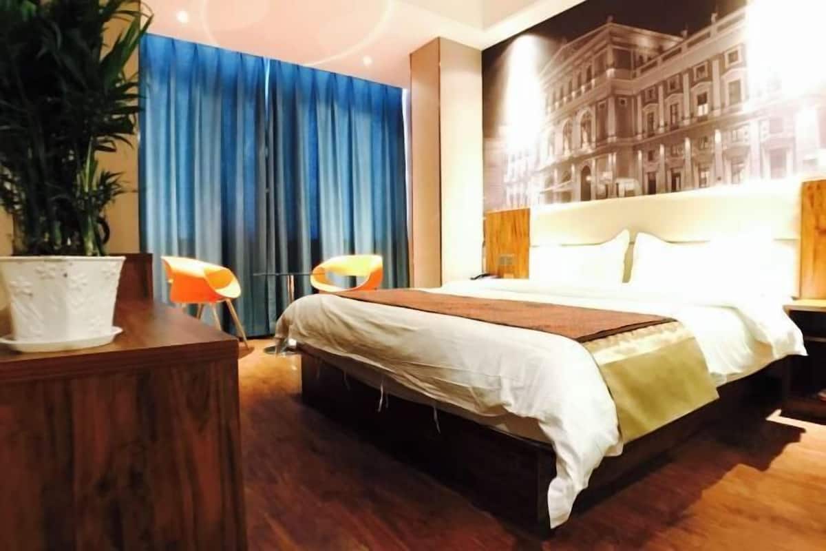 Una habitación de hotel con una cama grande, una cortina azul, una planta y una lámpara fijada a la pared.