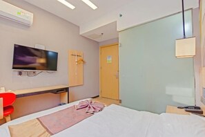 Une chambre d’hôtel avec un lit, un bureau, une télévision, une armoire et une porte.