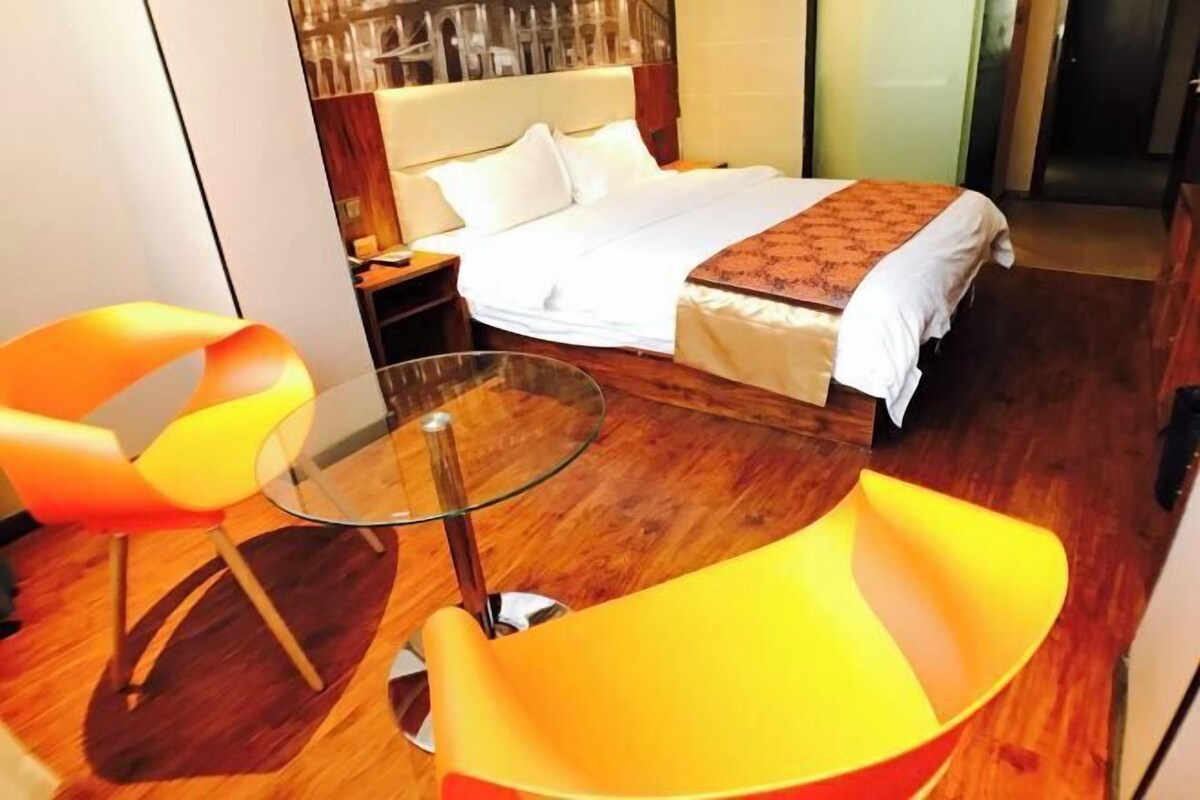 Une chambre d’hôtel avec un lit, une table en verre et deux chaises orange.