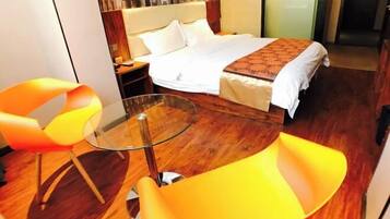 Quarto de hotel com uma cama, uma mesa de vidro e duas cadeiras laranja.